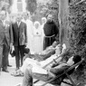 Mussolini e Bianchi ascoltano un medico, in piedi di fronte a dei pazienti, seduti su delle sdraio nel parco del sanatorio; alle loro spalle si scorgono infermiere, un frate e altre persone