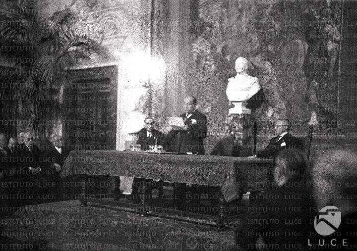 Benito Mussolini tiene un discorso, nella sala di un palazzo, in piedi ...