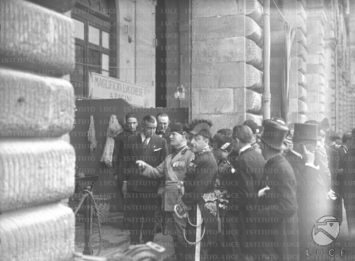 Mussolini, accompagnato da un folto gruppo di autorità, si sofferma ...