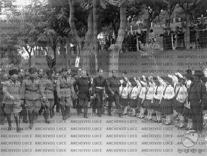 Mussolini avanza, con un folto gruppo di autorità politiche e militari ...