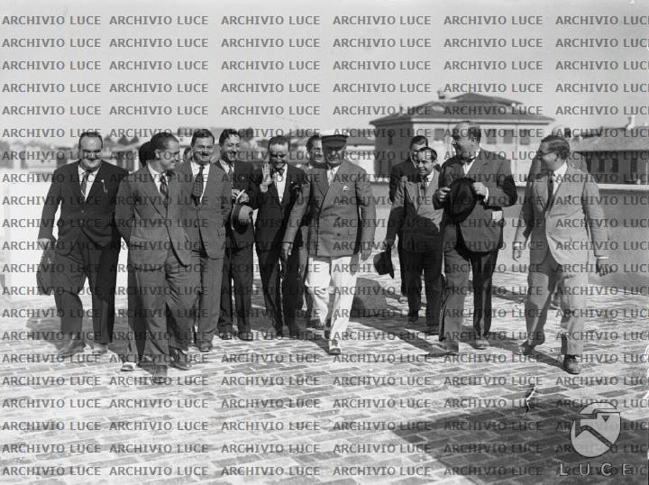 Mussolini, accompagnato da un gruppo di personalità, attraversa la ...