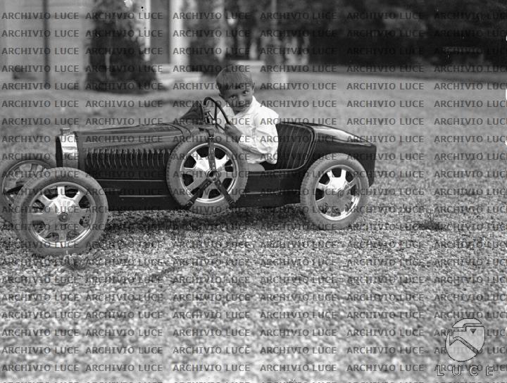 Romano Mussolini posa a bordo di una macchina giocattolo nel giardino ...