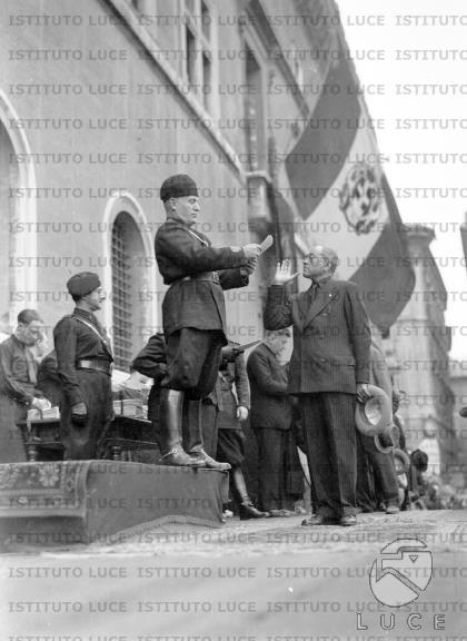 Un uomo mentre fa il saluto fascista davanti a Mussolini su un palco in ...