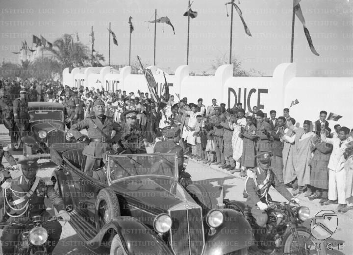 Bengasi: Mussolini e Balbo sfilano in automobile lungo una strada di ...