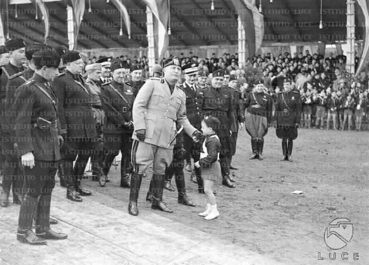 Mussolini, seguito da un folto gruppo di autorità in orbace, incontra ...