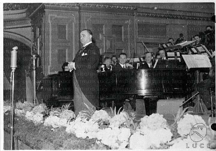 Beniamino Gigli sul palco durante la sua alle sue spalle parte dell'orchestra