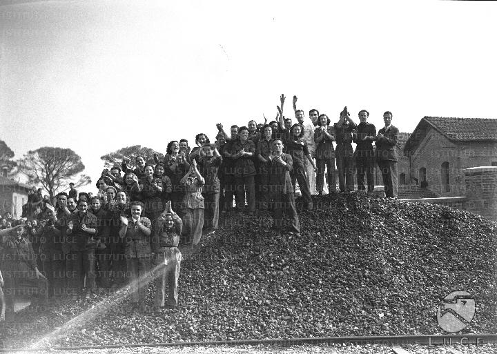Un gruppo di operaie e operai, in divisa, saluta Benito Mussolini ...