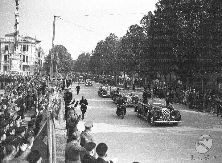 Benito Mussolini, in piedi sull'automobile scoperta, percorre una via ...