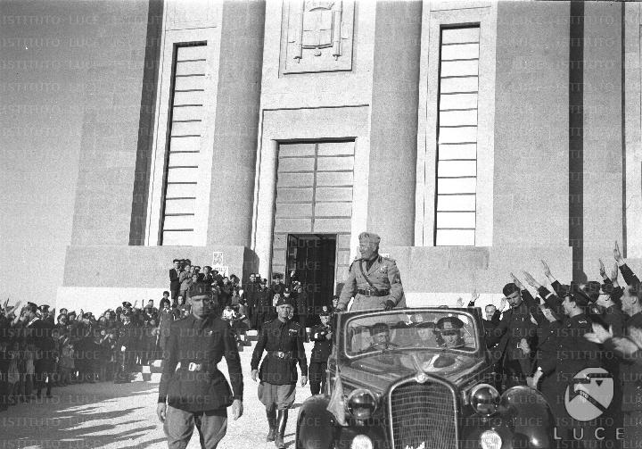 Mussolini, in piedi a bordo di un'automobile scoperta, si allontana da ...