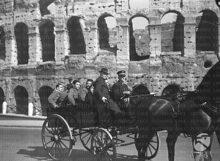 Un gruppo di mutilati di guerra compie un giro per Roma a bordo di una carrozza a cavalli e si sofferma nei pressi del Colosseo