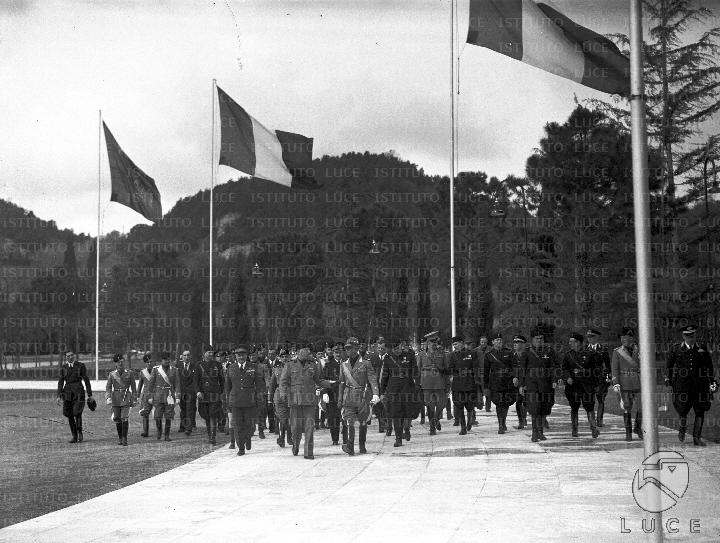 Mussolini, Ricci e un folto gruppo di personalità camminano in un viale ...