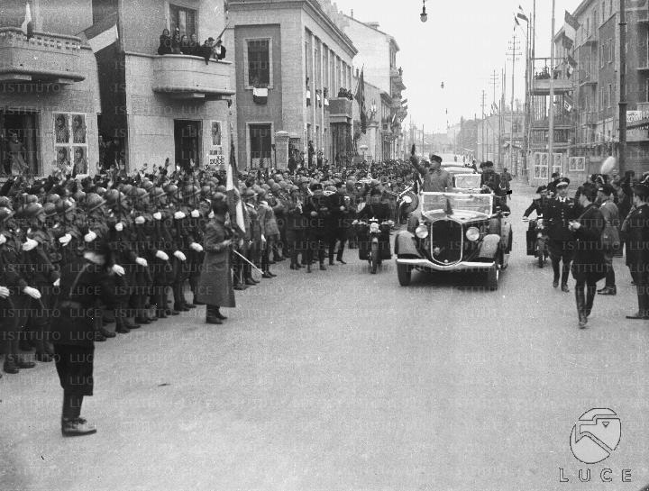 Mussolini, in piedi a bordo di un'automobile, fa il saluto fascista a ...