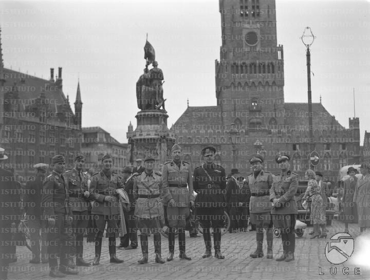 Autorità italiane e tedesche in posa nella piazza centrale di Bruges, sullo sfondo la folla e la Torre Civica