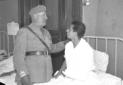 Il Duce parla con un ferito seduto sul letto; pian ...