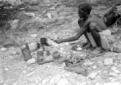 Un indigeno, accovacciato a terra, scalda del cibo ...