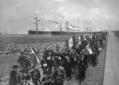 Processione di rurali italiani lungo un molo del p ...