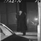 Erhard esce da un edificio. Totale, notturno