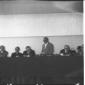 Un uomo sul palco legge un documento, altre person ...
